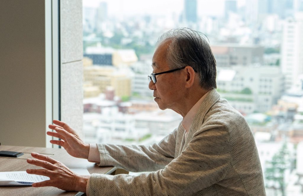窓際の席で手振りを交えて話す蓑茂壽太郎チーフディレクター